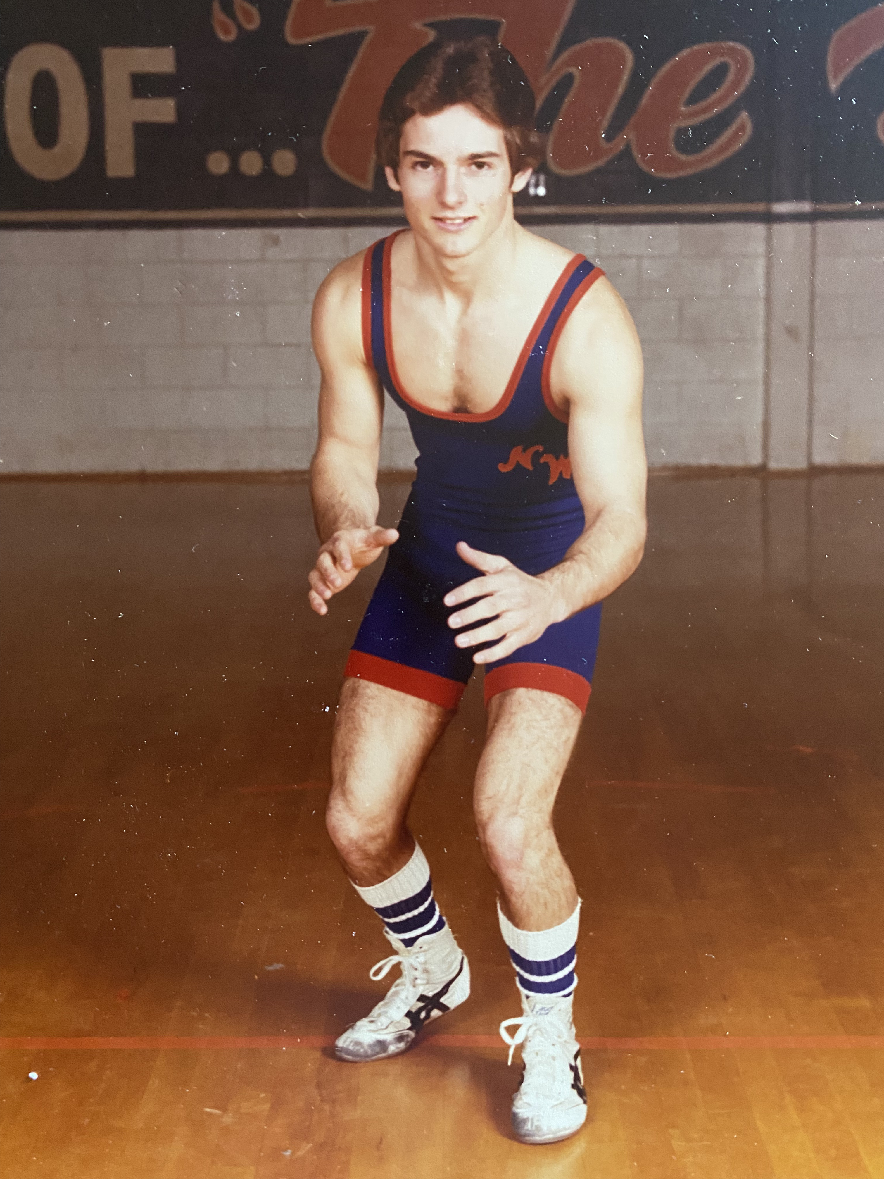 A young Travis Presley in his blue and red wrestling singlet, crouched in a ready stance on a gymnasium mat
