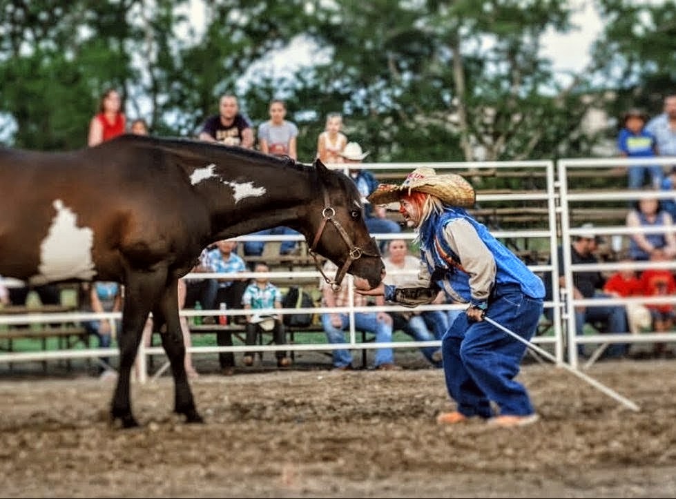 Travis Presley in full rodeo clown makeup and baggy gear performing an arena routine with his trick horse Sparky, dust kicking up under the lights